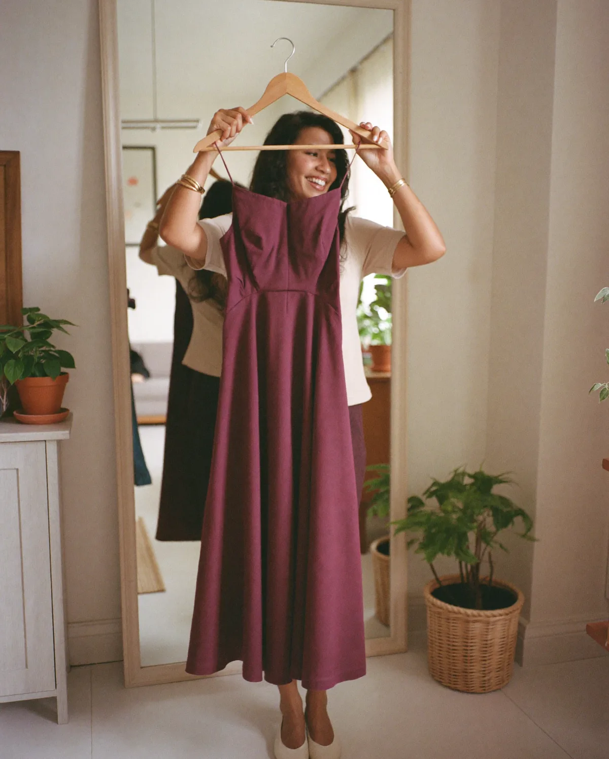 Woman at home holding up a burgundy midi dress on a hanger in front of a mirror