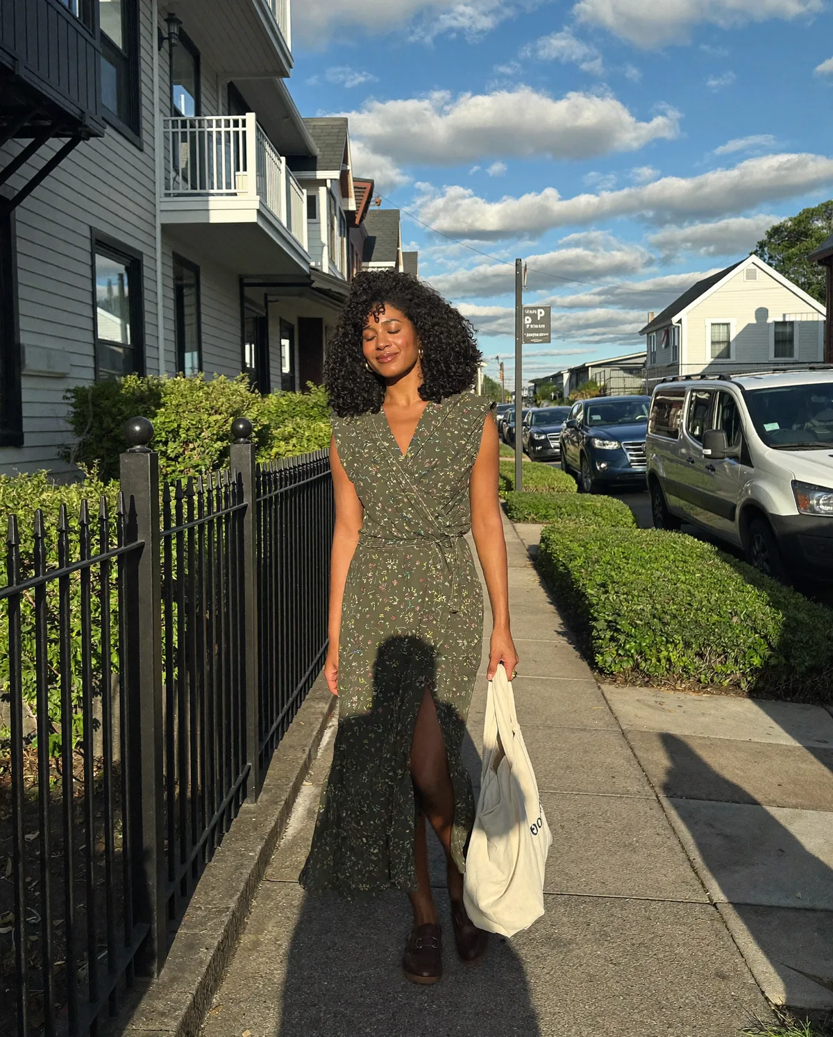 Woman wearing an olive floral wrap dress on a leafy neighbourhood sidewalk